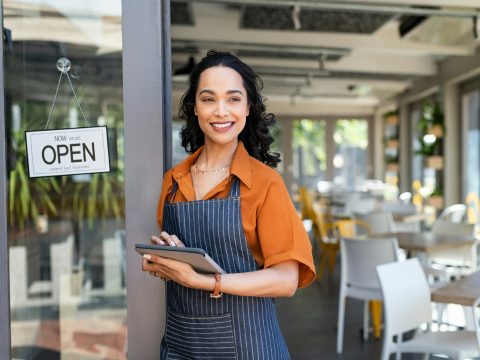 Small business entrepreneur at cafe entrance using digital tablet